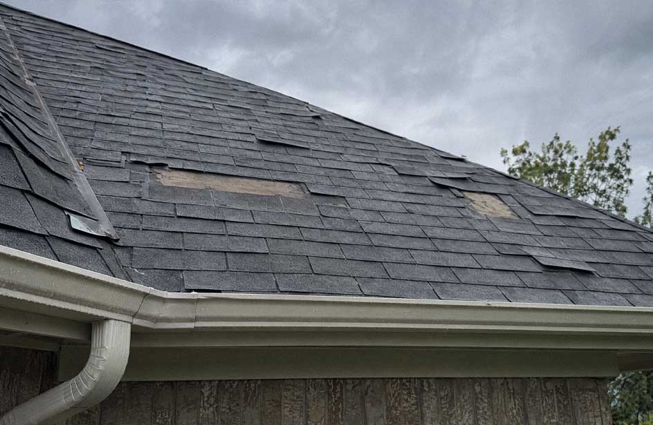 Close view of missing and displaced asphalt shingles after wind damage