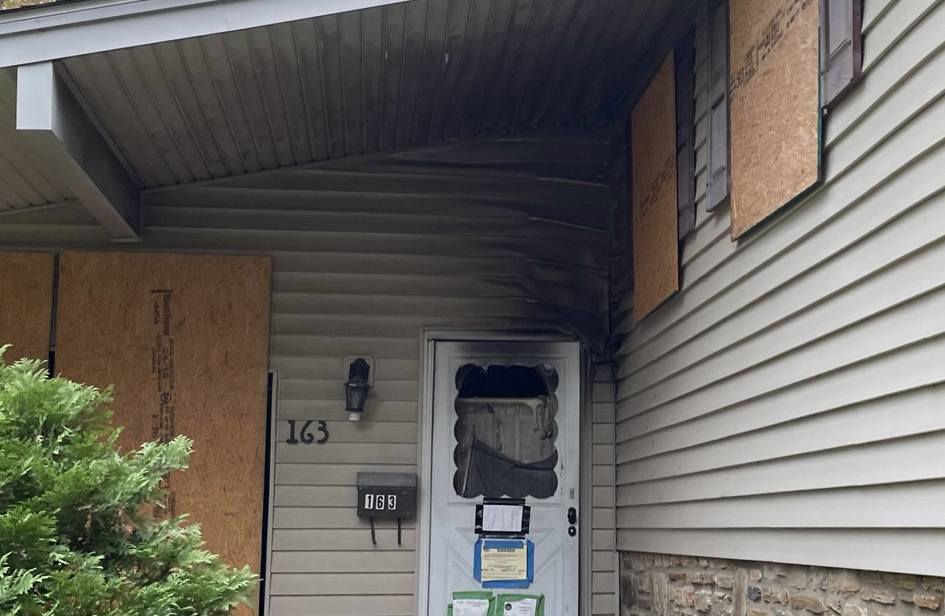 Yew Road home entrance showing plywood-protected windows, original siding and stone facade before exterior renovation