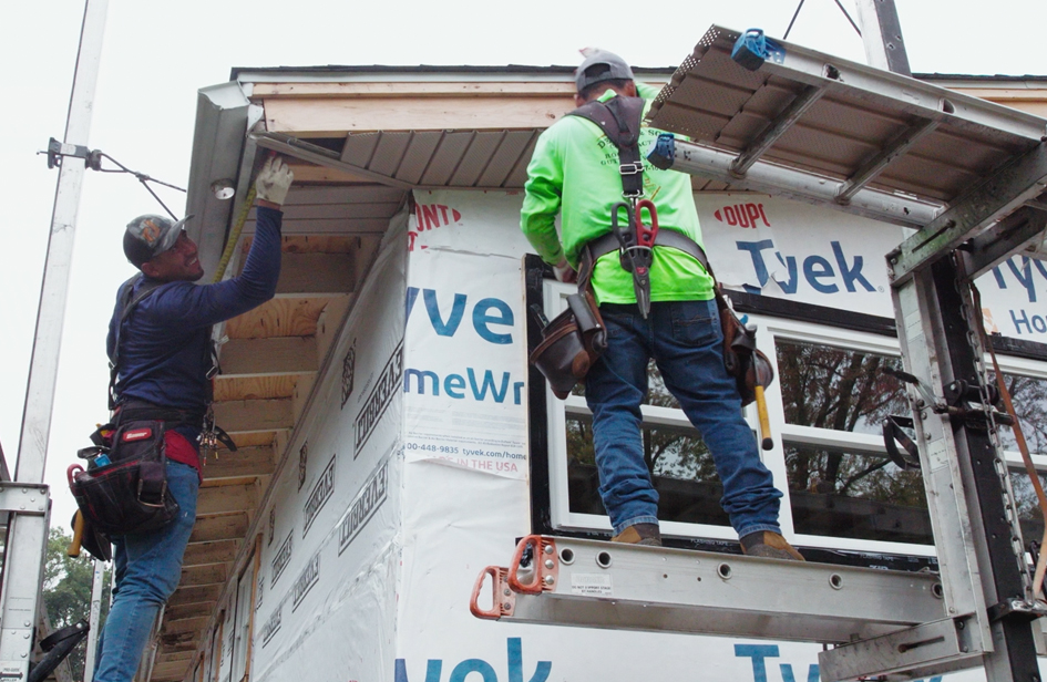 Two Sheppard Exteriors installers working from elevated platforms on soffit and roof edge trim near the housewrap